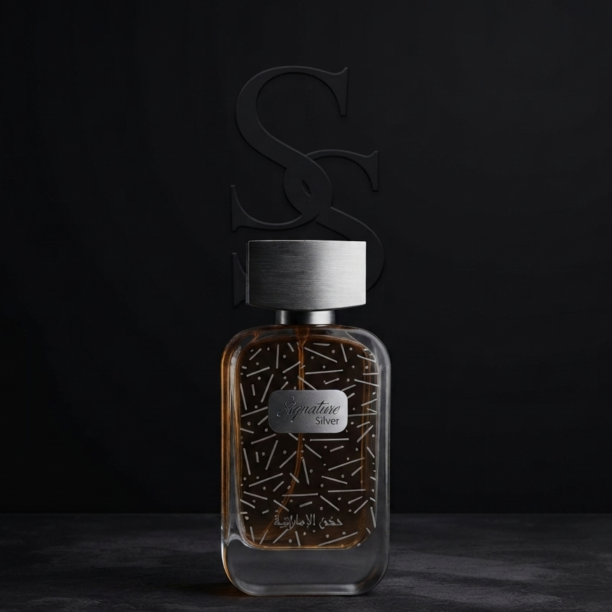 A rectangular glass perfume bottle with a brushed silver cap and a dark metallic cap silhouette featuring an interlocking 'S' and 'S' design. The bottle contains an amber-brown liquid with a gold geometric pattern on the front label. SHE GLOW