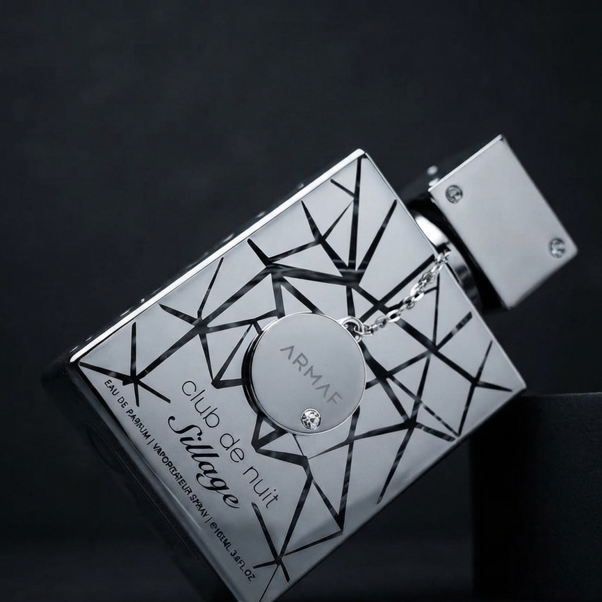 Armaf Club de Nuit Village perfume bottle with a silver and black geometric pattern, resting on a dark surface. SHE GLOW