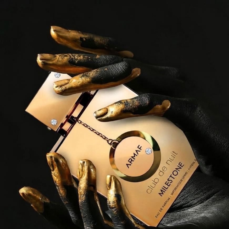 A perfume bottle labeled ARMAF club de nuit MILESTONE is held between two black-gloved hands with long, metallic gold nails against a black background. SHE GLOW