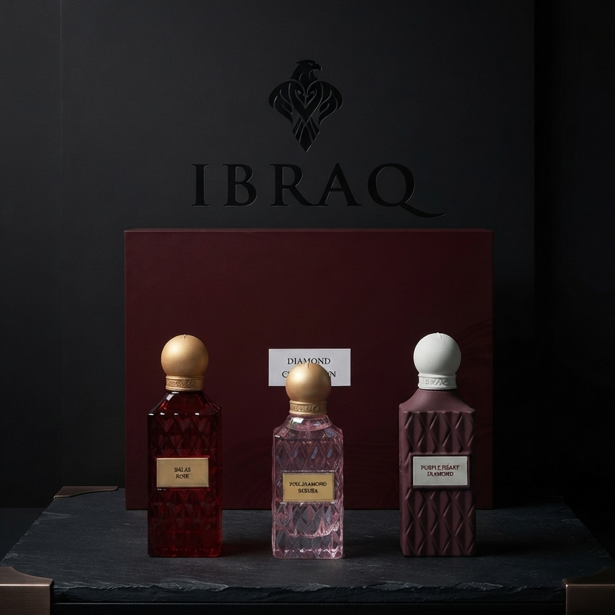 Three perfume bottles from the brand IBRAQ displayed on a dark slate tray in front of a dark red presentation box. The bottles contain deep red, pink, and plum-colored liquids and are topped with gold and white caps. SHE GLOW
