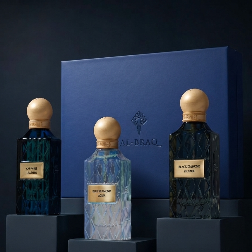 Three Al-Braq perfume bottles displayed on dark pedestals in front of a blue box. The bottles are faceted crystal in deep blue, teal, and dark blue-green tones, with round gold caps and gold labels reading 'AL-BRAQ' and 'SAPPHIRE NOTE', 'BLUE RAINBOW NOTE', and 'BLACK NOTE'.