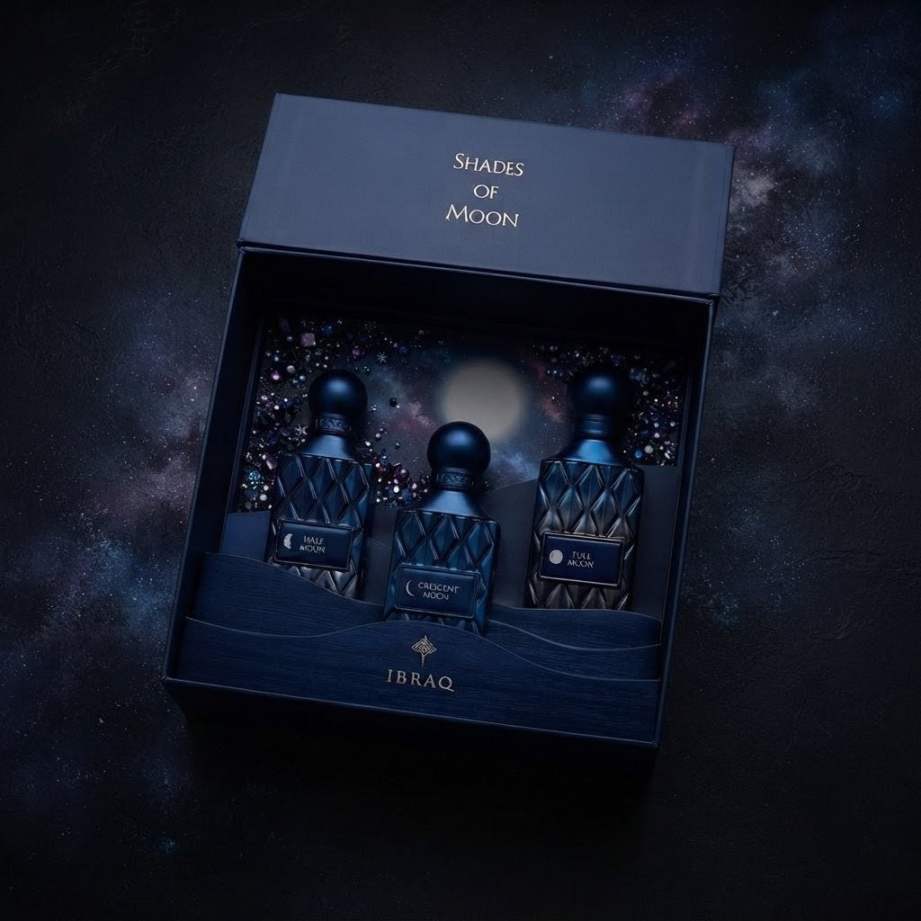 A dark navy presentation box labeled 'Shades of Moon' and 'IBRAQ' contains three matching dark textured perfume bottles arranged in a galaxy-themed interior. The set is photographed from above on a dark, starry background. SHE GLOW