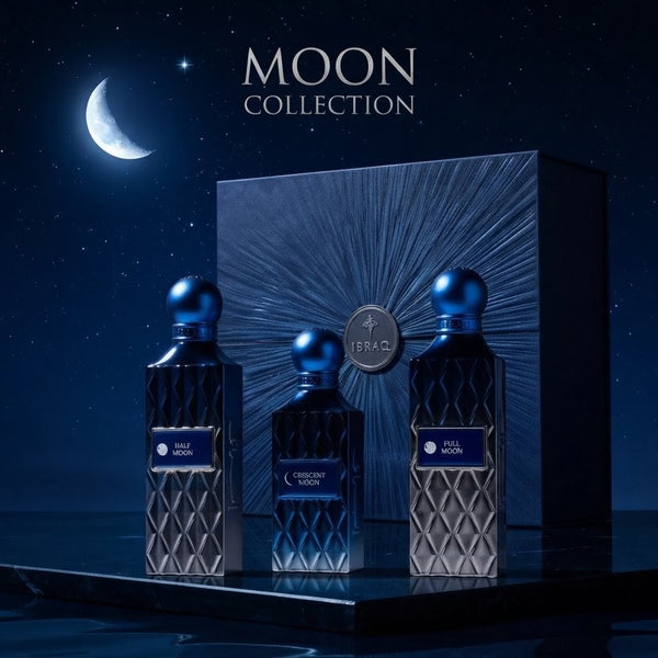 Three fragrance bottles from the Israel Air Force Moon Collection are displayed in front of a matching box under a night sky with a crescent moon. The bottles and box are dark blue with metallic blue caps and textured diamond-patterned fronts. SHE GLOW 