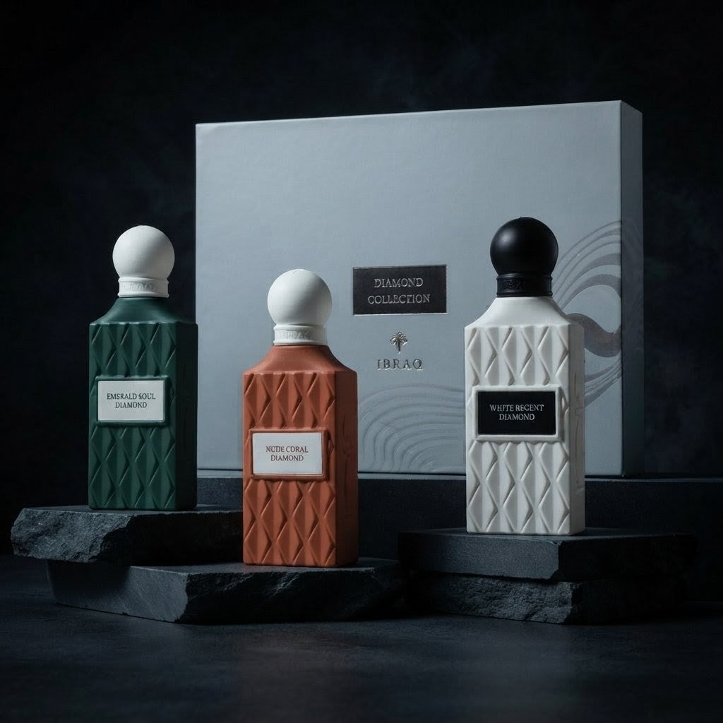 Three textured perfume bottles from the Delicio Collection by J'EAU are displayed on dark stone pedestals in front of a large presentation box. The bottles are colored emerald green, terracotta orange, and matte white, with white, silver, and black caps respectively. SHE GLOW