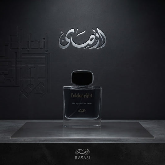 A clear rectangular perfume bottle with a black cap sits centered on a metallic platform against a dark gray background. Arabic script branding appears above and below the bottle, with the brand name Rasasi visible at the bottom. SHE GLOW 