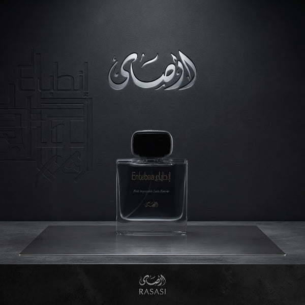 A clear rectangular perfume bottle with a black cap sits centered on a metallic platform against a dark gray background. Arabic script branding appears above and below the bottle, with the brand name Rasasi visible at the bottom. SHE GLOW 