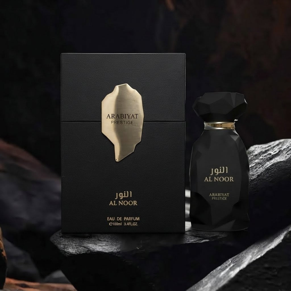 Arabiyat Noor Eau de Parfum shown with its black rectangular box and faceted black bottle, both featuring gold lettering, set against a dark rocky background. SHE GLOW