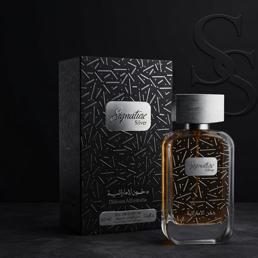 A perfume bottle with amber liquid and a silver cap stands in front of its black patterned box on a dark studio surface. The labels read Signature Series, and Arabic text is visible on both the bottle and box. SHE GLOW 
