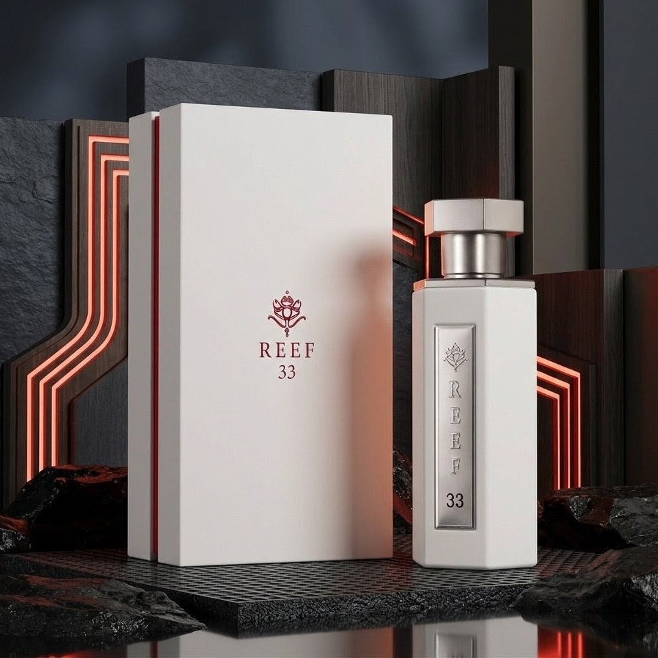 A white rectangular perfume box and matching bottle labeled REEF 33, displayed on a dark textured surface with glowing red geometric background accents. SHE GLOW