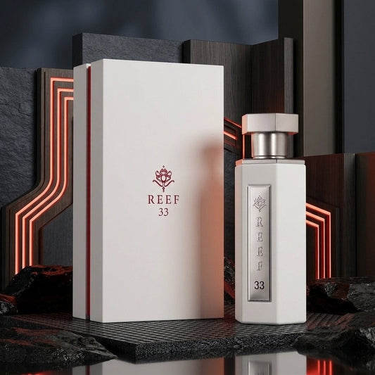 A white rectangular perfume box and matching bottle labeled REEF 33, displayed on a dark textured surface with glowing red geometric background accents. SHE GLOW