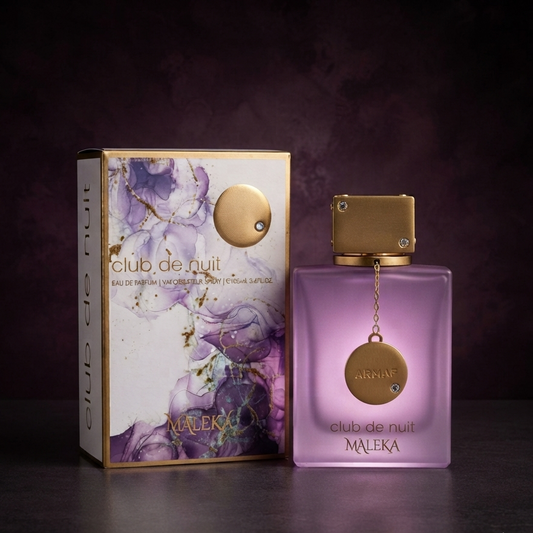 A bottle of MALEKA Club de Nuit perfume with a translucent lavender-purple glass body and a gold cap, standing next to its matching illustrated box on a dark surface against a dark purple background. SHE GLOW 