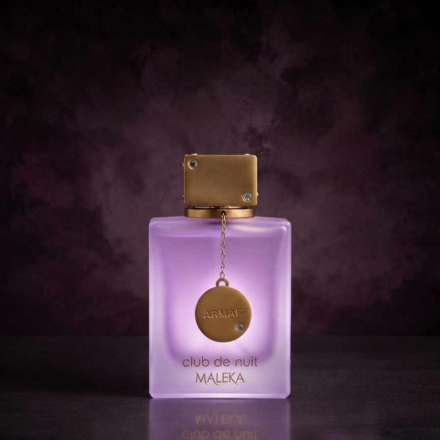A bottle of MALEKA Club de Nuit fragrance with a frosted lavender-purple glass body and a metallic gold cap, featuring a gold circular pendant charm on a dark, moody background. SHE GLOW