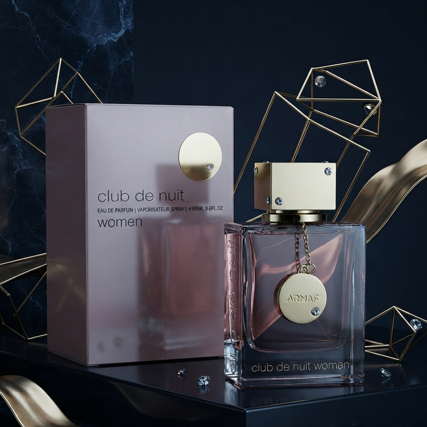 Club de Nuit Women perfume bottle and its matching box, styled on a dark reflective surface with gold geometric wireframe props and metallic ribbon accents. SHE GLOW