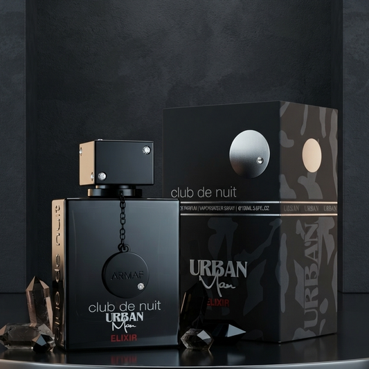 Urban Men Club de Nuit perfume bottle and its packaging box displayed on a reflective black surface against a dark gray background. SHE GLOW 