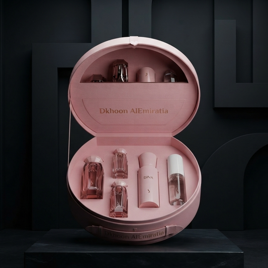 An open round pink presentation case displayed on a dark pedestal, containing several small pink and clear cosmetic bottles. The inside lid is printed with the text 'Dkhoon AlEmiratia'. SHE GLOW