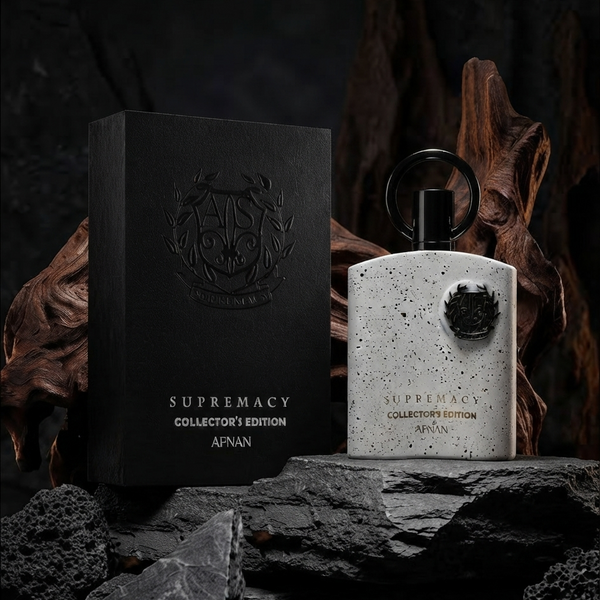 A perfume bottle and its packaging box from AFNAN Supremacy Collector's Edition, styled on dark rocks with driftwood against a dark background.           SHE GLOW