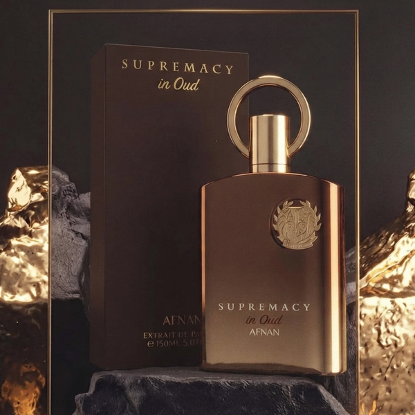 A bottle of Afanar 'Supremacy in Oud' perfume with its matching dark brown box, set against a dark background with textured gold mountain props. SHE GLOW