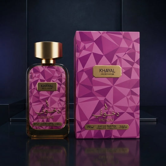 Khayal Dikhoni Eau de Parfum bottle with a gold cap next to its geometric pink and purple box packaging, set against a dark reflective background. SHE GLOW 