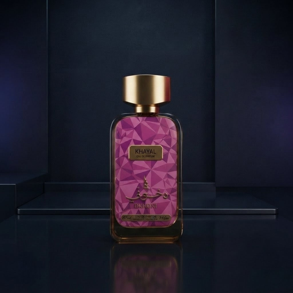 A rectangular perfume bottle with a geometric pink pattern and a metallic gold cap, labeled KHAYAL, set against a dark navy blue background with a reflective surface. SHE GLOW 