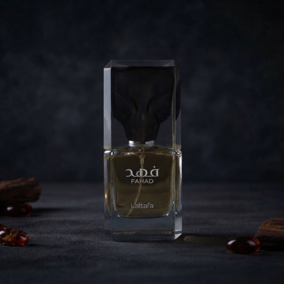 A rectangular glass perfume bottle with a dark cap, filled with amber-toned liquid, standing on a dark surface against a dark background. The bottle has a clear geometric front and back, with the brand name 'PANAD' and scent name 'Latafa' visible on the front. SHE GLOW ✨