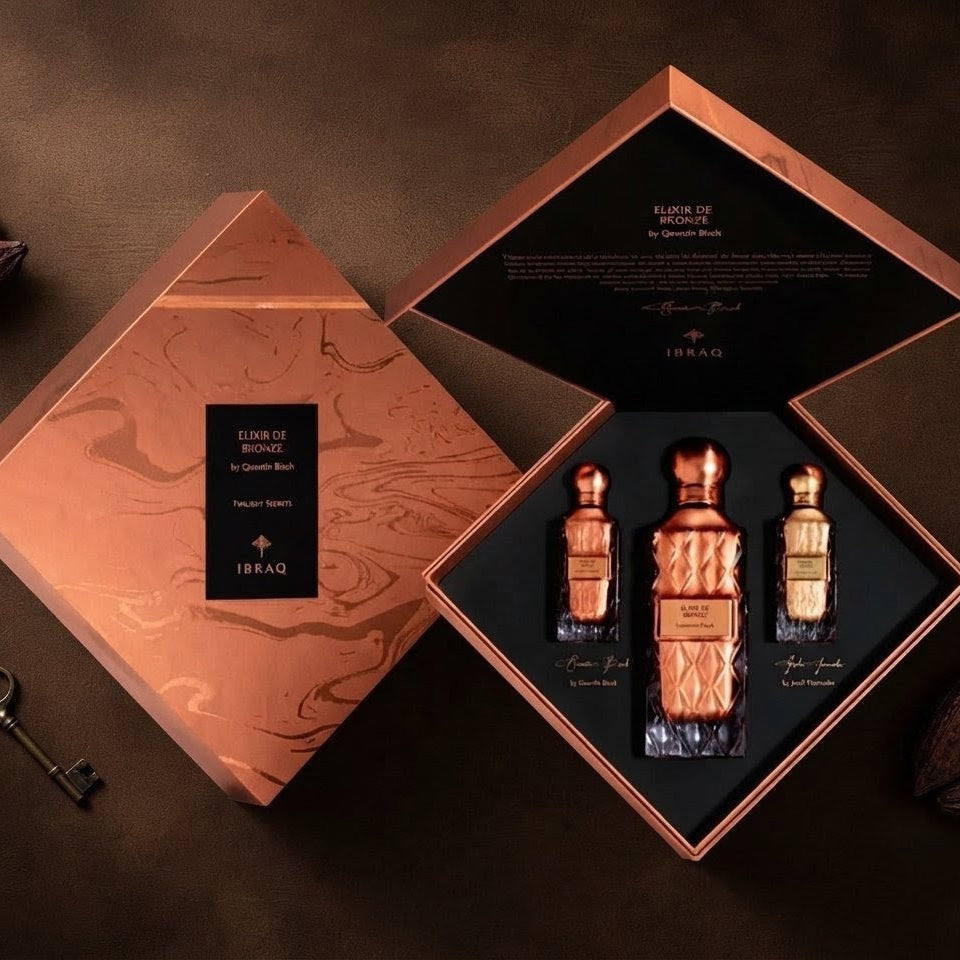 A luxury fragrance gift set from 1840, featuring three ornate copper-toned perfume bottles displayed inside an open matching geometric box, alongside the closed lid. The set is styled on a dark brown textured surface with decorative cocoa beans and a vintage key. 
SHE GLOW ✨