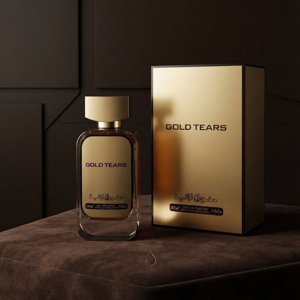 A bottle of Gold Tears fragrance with a matching metallic gold box, displayed on a dark brown velvet surface against a dark brown paneled background.SHE GLOW ✨