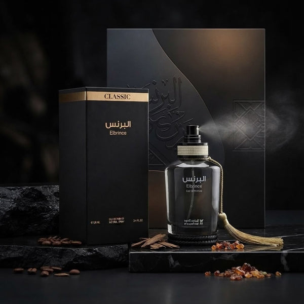 A dark glass perfume bottle labeled 'Elmoss' with Arabic text, shown next to its black packaging box with gold accents. The bottle is styled on a dark marble surface with coffee beans and spices, with a matching black presentation box and backdrop behind it. SHE GLOW ✨