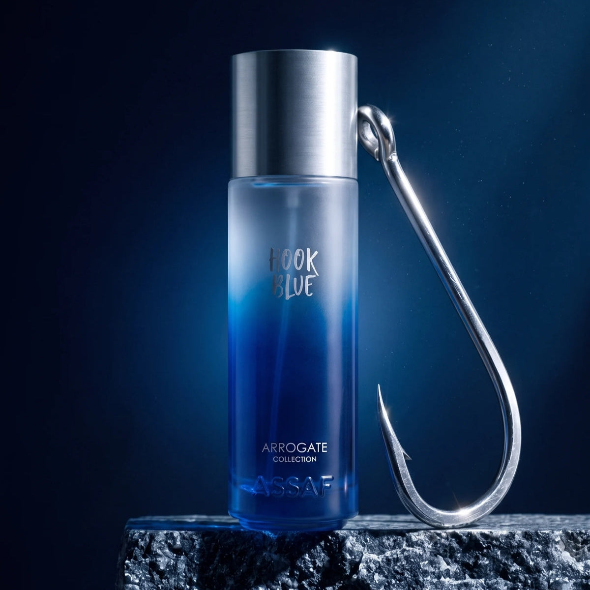 A blue cylindrical fragrance bottle labeled 'HOOK BLUE' and 'ASSAF' stands on a dark textured surface with a large metallic hook beside it against a deep blue background. SHE GLOW