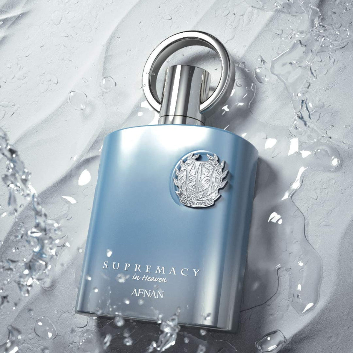 A bottle of Afnan Supremacy de Parfum with a metallic light blue body and silver cap, set against a dynamic background of water splashes and droplets. SHE GLOW 